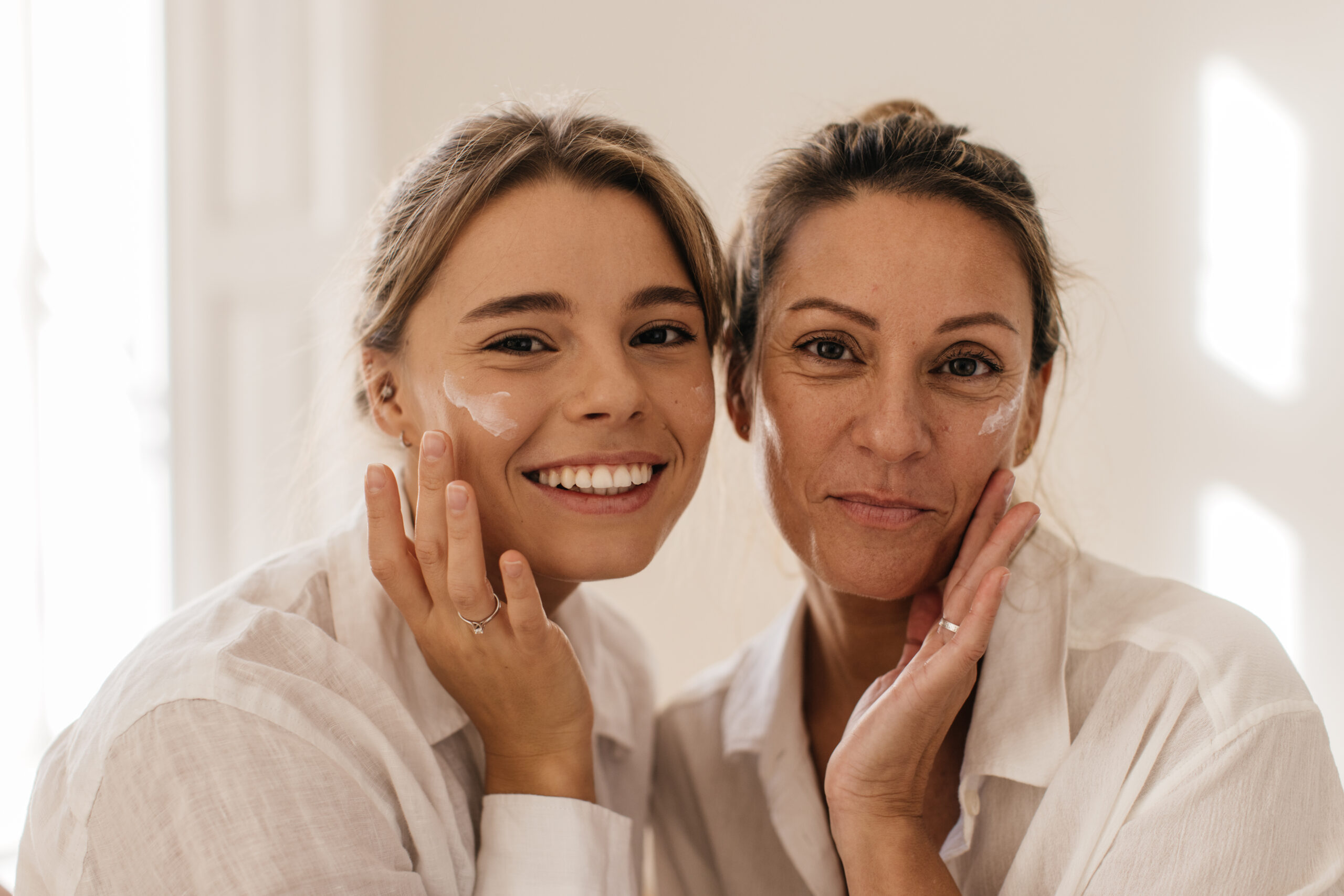 close up two cute caucasian women smearing their face with cream looking camera white background beauty youth concept